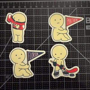 May include: Four die-cut stickers featuring a pale yellow cartoon character. One wears a red and blue hockey jersey, one holds a red pennant with the text PANTHERS, one holds a blue pennant with the text FLORIDA, and one holds a hockey stick.