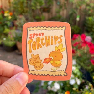 Pode incluir: Um adesivo de um saco de batatas fritas de desenho animado com o texto "Spicy Torchchips" na frente. Um pássaro de desenho animado com chamas saindo de sua boca está segurando uma batata frita.