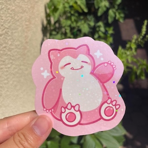 May include: Pink glitter sticker of a cartoon pink Pokemon character with a white belly and a happy expression. The character has a large, round body and small arms and legs.