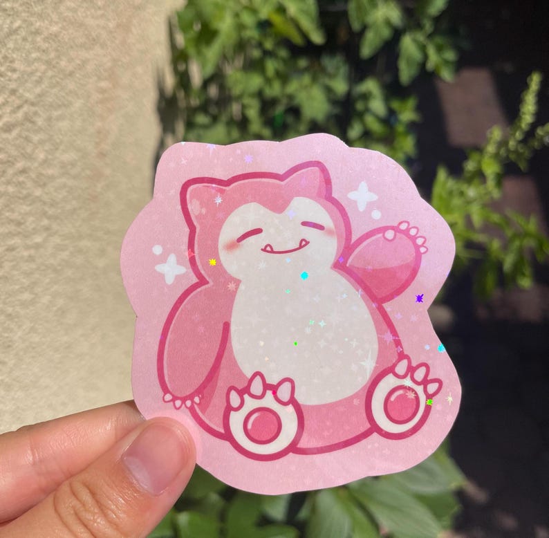 May include: Pink glitter sticker of a cartoon pink Pokemon character with a white belly and a happy expression. The character has a large, round body and small arms and legs.