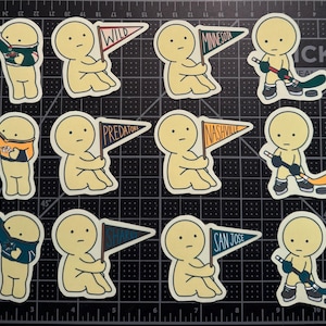 May include: A collection of twelve die-cut stickers featuring cartoon figures in various poses. Some figures hold pennants labeled Wild, Minnesota, Predators, Nashville, Sharks, and San Jose, while others wear hockey jerseys or hold hockey sticks.