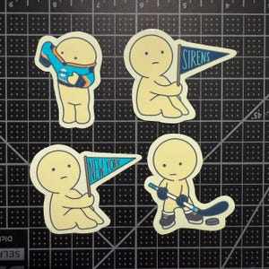 May include: Four die-cut stickers featuring pale yellow cartoon figures. One wears a blue and orange hockey jersey, one holds a blue pennant labeled SIRENS, one holds a blue pennant labeled NEW YORK, and one holds a hockey stick with a puck.