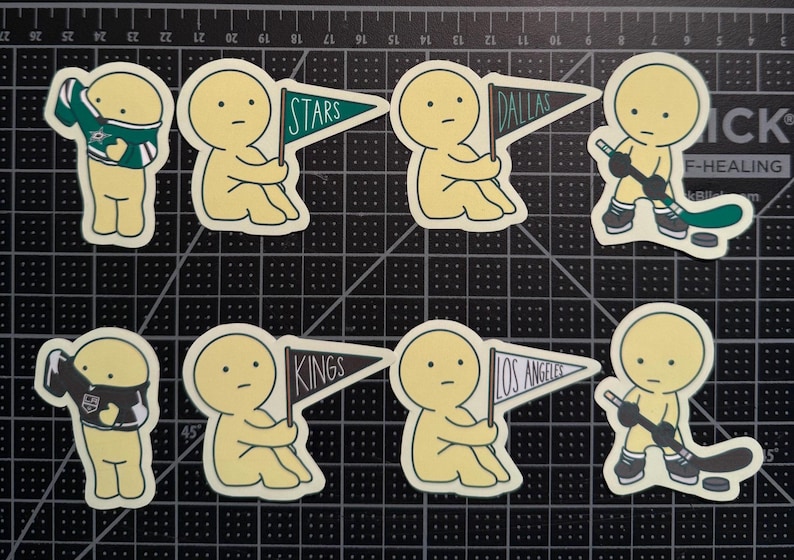 May include: A set of eight die-cut stickers featuring pale yellow cartoon figures. Four figures hold pennants labeled Stars, Dallas, Kings, and Los Angeles. Two figures wear hockey jerseys, and two figures hold hockey sticks with pucks.