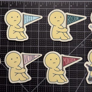 May include: Eight die-cut stickers featuring yellow cartoon figures. Two figures wear hockey jerseys, two hold hockey sticks with pucks, and four hold triangular pennants labeled FLEET, BOSTON, VICTOIRE, and MONTREAL in various colors.