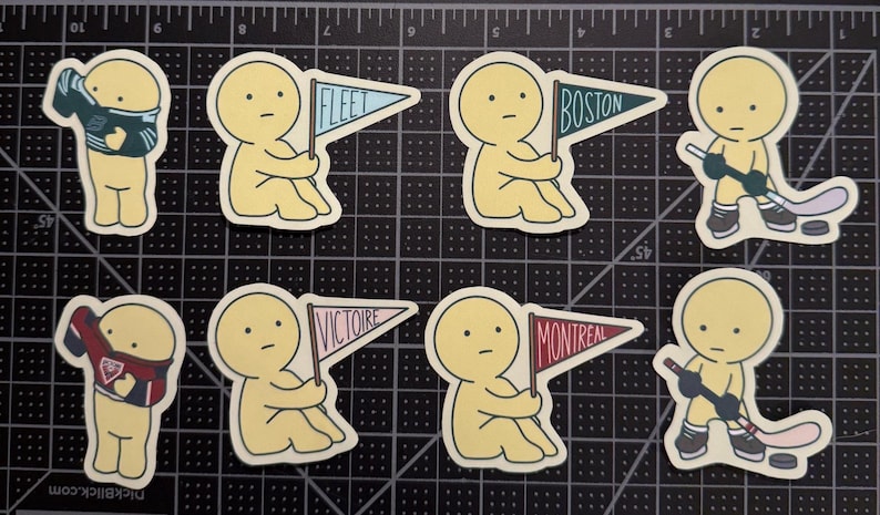 May include: Eight die-cut stickers featuring yellow cartoon figures. Two figures wear hockey jerseys, two hold hockey sticks with pucks, and four hold triangular pennants labeled FLEET, BOSTON, VICTOIRE, and MONTREAL in various colors.