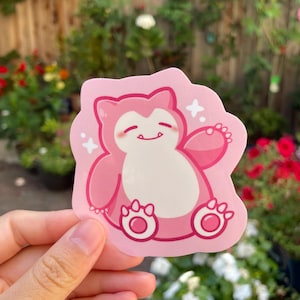May include: Pink and white cartoon sticker of a pink Snorlax Pokemon character with a white smile and white stars in the background.