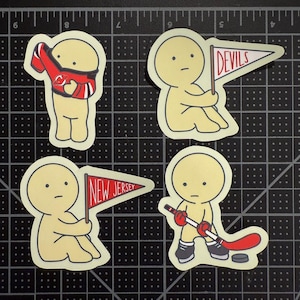 May include: Four die-cut stickers featuring a pale yellow cartoon character. One wears a red and black hockey jersey, two hold triangular pennants labeled "DEVILS" and "NEW JERSEY" in red text, and one holds a hockey stick with a puck nearby.