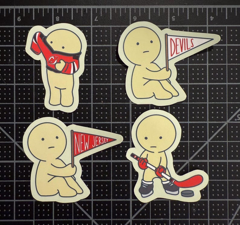 May include: Four die-cut stickers featuring a pale yellow cartoon character. One wears a red and black hockey jersey, two hold triangular pennants labeled "DEVILS" and "NEW JERSEY" in red text, and one holds a hockey stick with a puck nearby.