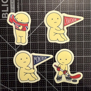 May include: Four die-cut stickers featuring a yellow cartoon character. One wears a red, white, and blue hockey jersey. Another holds a red pennant with the text CANADIENS. A third holds a blue pennant with MONTREAL. The fourth holds a hockey stick.