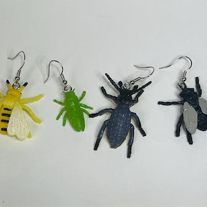 Puede incluir: Cuatro pares de pendientes de insectos. Los pendientes están hechos de plástico y presentan una abeja, un saltamontes, un escarabajo y una mosca. Los pendientes son de color plateado y tienen un cierre de gancho.