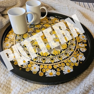Può includere: Un vassoio nero con un design a mandala bianco e giallo con un motivo a nido d'ape e margherite. Due tazze in ceramica bianca sono sul vassoio.