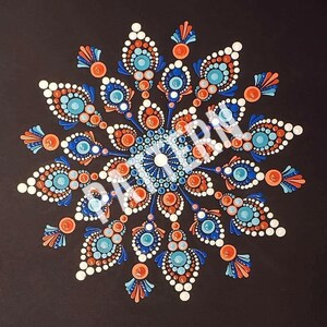 May include: A symmetrical mandala design on a black background. The artwork features a circular pattern with blue, orange, and white dot details. The design is intricate and detailed, with a central focus and radiating elements.