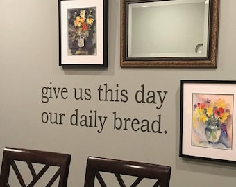 May include: A wall with a framed mirror and two framed watercolor paintings of flowers in vases. The wall also has a quote that reads "give us this day our daily bread."