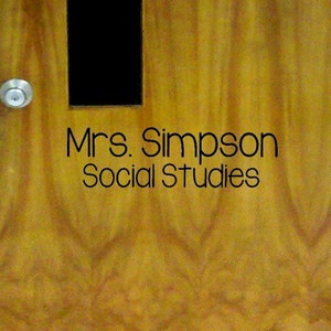 May include: A wooden door with a small window and a silver door knob. The door is labeled "Mrs. Simpson Social Studies".
