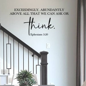 May include: A black and white wall decal with the quote "Exceedingly, abundantly above all that we can ask or think." Ephesians 3:20. The decal is placed on a white wall in a dining room with a black and gray table and white chairs.