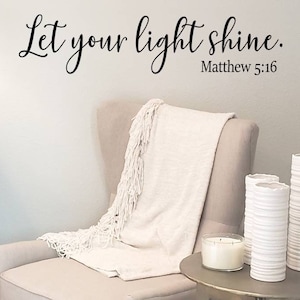 May include: A white armchair with a white throw blanket and a side table with three white ceramic vases and a candle. The wall behind the chair has a black calligraphy quote that reads "Let your light shine. Matthew 5:16"
