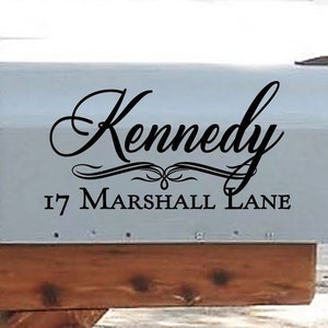 May include: A light gray mailbox with the name "Kennedy" in elegant black script, along with the address "17 Marshall Lane." The mailbox is mounted on a wooden post.