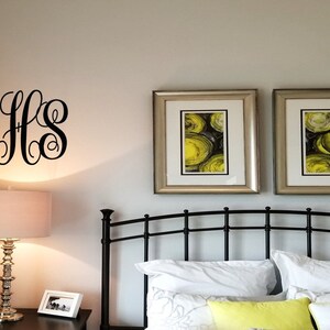 May include: A black metal monogram with the letters "SHS" on a white wall above a bed with a black metal headboard. Two framed pictures with yellow and black abstract art hang above the headboard.