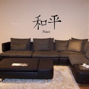 May include: A black sectional sofa with grey cushions and a black leather ottoman. The wall behind the sofa has a black and white wall decal with the Chinese characters for "peace" and the word "Peace" written below.