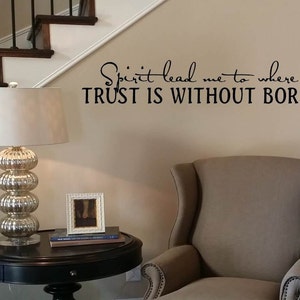 May include: A beige armchair with a black and white framed picture on a black end table with a lamp. The wall behind the chair has a black vinyl decal with the text "Spirit lead me to where my TRUST IS WITHOUT BORDERS".