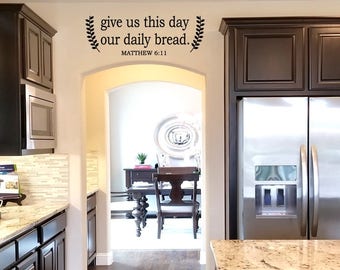 May include: A kitchen with dark wood cabinets, a stainless steel refrigerator, and a white wall with a black vinyl decal that reads "give us this day our daily bread. Matthew 6:11".