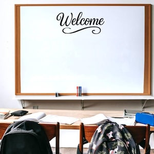 May include: A classroom scene featuring a large white board with a brown wooden frame. The word "Welcome" is written in elegant black script. A desk with books, a pencil case, and backpacks is in front of the board.