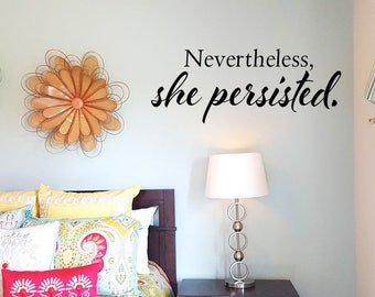 May include: A bedroom with a bed featuring colourful pillows and a quote on the wall that reads "Nevertheless, she persisted."