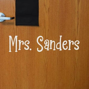 May include: A wooden door with a nameplate that reads "Mrs. Sanders".