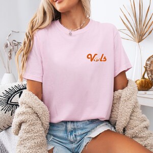 May include: A pink t-shirt with the word "Vols" in orange lettering and a football graphic.