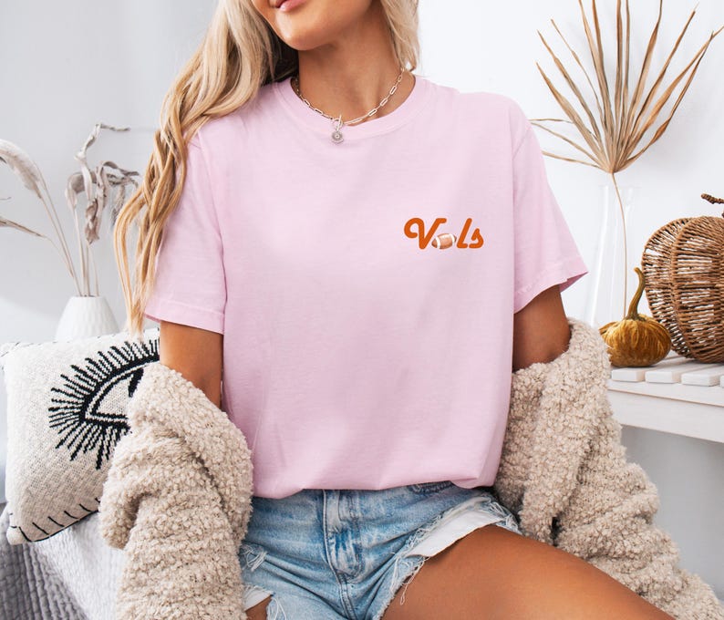 May include: A pink t-shirt with the word "Vols" in orange lettering and a football graphic.
