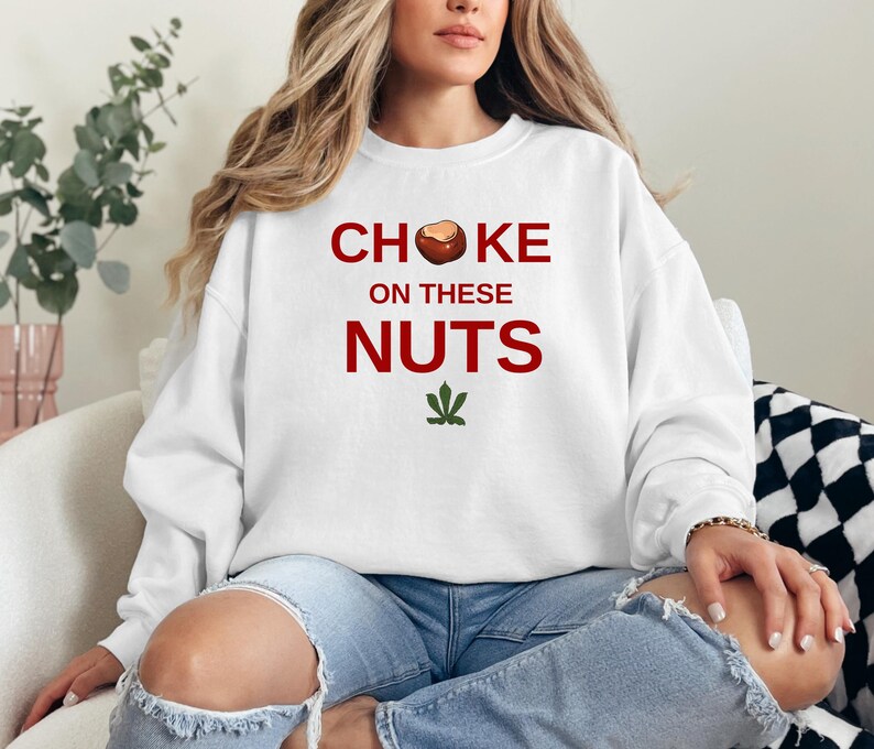 May include: White sweatshirt with the text "CHOKE ON THESE NUTS" in red letters and a brown nut graphic. A green marijuana leaf is below the text.