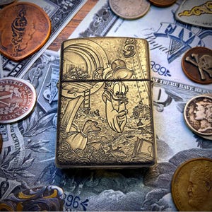 May include: A gold-colored metal lighter featuring a detailed engraving of a cartoon duck holding a money bag, surrounded by coins and a treasure chest. The lighter is set against a backdrop of currency and antique coins.
