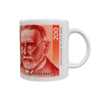 May include: White ceramic mug featuring a portrait of a man with glasses and a beard, reminiscent of a German banknote. The mug has the text "200 ZWEIHUNDERT DEUTSCHE MARK" in orange and white. The serial number "AD4829120N7" is also visible.