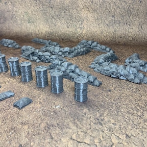 May include: A collection of grey miniature barrels, sandbags, and barricades. These 3D-printed models are designed for tabletop gaming or model displays. The set includes several barrels, sandbag walls, and small barricades, all in a neutral grey colour.