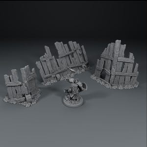 Op de afbeelding: Een miniatuurscène met drie verweerde houten heksecties en een klein beeldje. De hekken zijn grijs en zien er verouderd uit, met gebroken planken en een ruwe textuur. Het beeldje staat in een gevechtshouding en houdt een wapen en een schild vast.