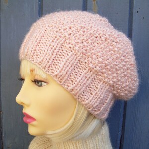 May include: A pink knitted beanie hat with a slouchy style. The hat is made of a soft, textured yarn.