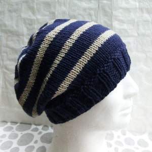 May include: A blue and beige striped knit beanie hat. The hat is folded down and has a slouchy fit.