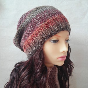 May include: A slouchy beanie hat with a gradient of grey, burgundy, and orange. The hat is knitted with a textured stitch.