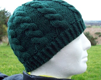 May include: A dark green knitted beanie with a cable knit design. The hat is made of a thick yarn and has a ribbed brim. The beanie is displayed on a white mannequin head.