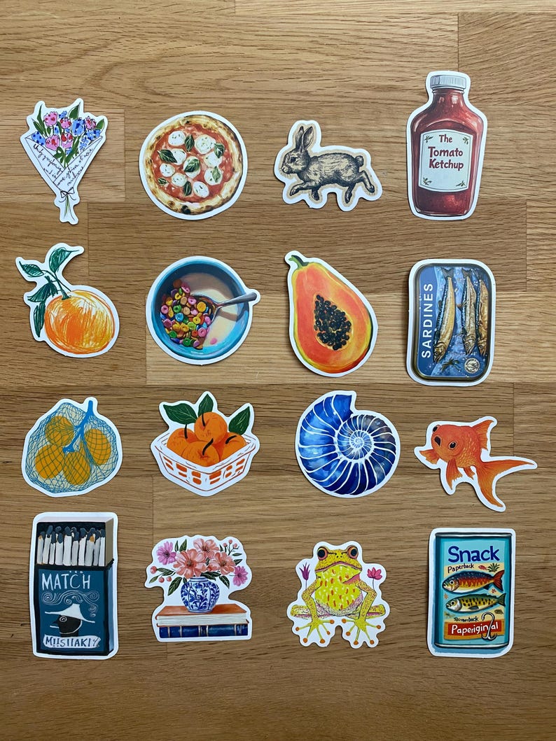Op de afbeelding: Een verzameling stickers met verschillende illustraties. Inbegrepen zijn een pizza, een konijn, een ketchupfles, een kom ontbijtgranen, een papaja, een blikje sardines, een goudvis, een kikker en een doosje lucifers.