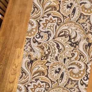 May include: A black and gold paisley table runner with a floral pattern. The runner is made of fabric and has a soft, luxurious feel.