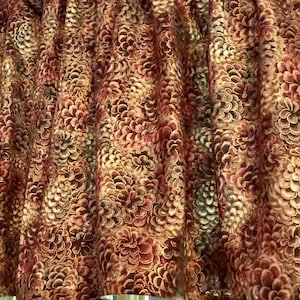 May include: Close-up of a red and gold fabric with a floral pattern. The fabric has a textured, almost 3D look, with the flowers appearing to be raised.