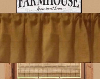 May include: A rectangular sign with a white background and black text reading FARMHOUSE home sweet home, positioned above a gathered mustard yellow fabric curtain and a wooden window frame with a light brown woven bamboo shade inside the window.