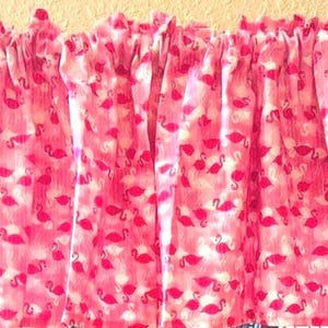 May include: Pink valance with a white flamingo pattern. The valance is made of a soft, lightweight fabric and has a ruffled edge.