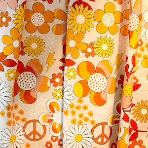 May include: A white fabric with a repeating pattern of orange, yellow, and pink flowers. The flowers have a retro 1970s style.