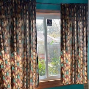 May include: Two patterned curtains with a geometric design in shades of brown, teal, and gold frame a window. The curtains are hanging on a rod above the window. The window looks out onto a yard with a house and trees.