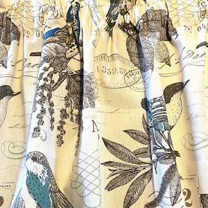 May include: Cream-colored fabric curtain with a repeating pattern of birds, leaves, and botanical illustrations in shades of brown and teal. The design includes script and postal stamp motifs, creating a vintage aesthetic.