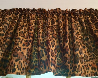 Puede incluir: Una cenefa de ventana con un estampado de leopardo en tonos marrón, beige y negro. La tela está fruncida en la parte superior con un bolsillo para barra, creando pliegues verticales que cuelgan a lo largo del ancho de la cortina.