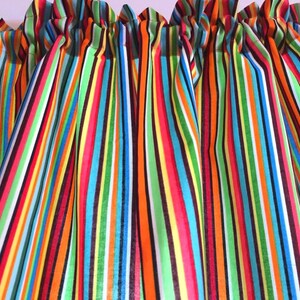 May include: A window valance featuring a vibrant vertical striped pattern in bright shades of orange, lime green, turquoise, yellow, dark brown, and white. The fabric is gathered at the top with a rod pocket header, creating soft, cascading folds.