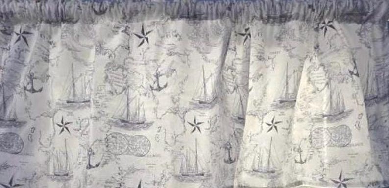 Pode incluir: Uma sanefa de janela branca com uma estampa n&aacute;utica repetitiva em azul escuro. O padr&atilde;o inclui ilustra&ccedil;&otilde;es de veleiros, &acirc;ncoras, rosas dos ventos e mapas. O tecido &eacute; franzido no topo com um bolso para var&atilde;o de cortina.